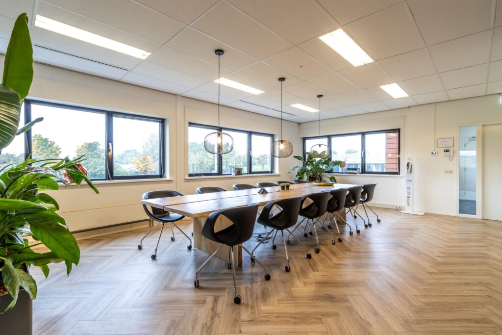 Moderne vergaderruimte aan de Lage Biezenweg met lange houten tafel, zwarte stoelen, grote ramen en hanglampen.